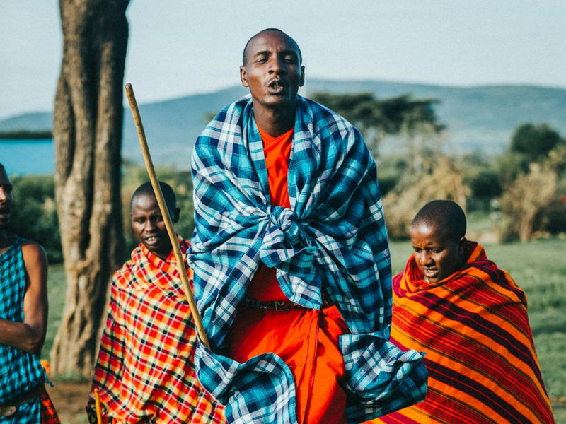 Two Maasai men in traditional dress standing beside an acacia